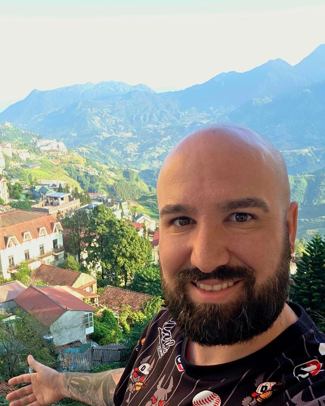 Manu lächelt in die Kamera, hinter ihm Berge und Häuser in Sapa, Vietnam